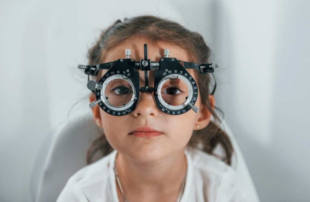Cute little girl is in ophthalmology clinic with special tool on eyes getting tested