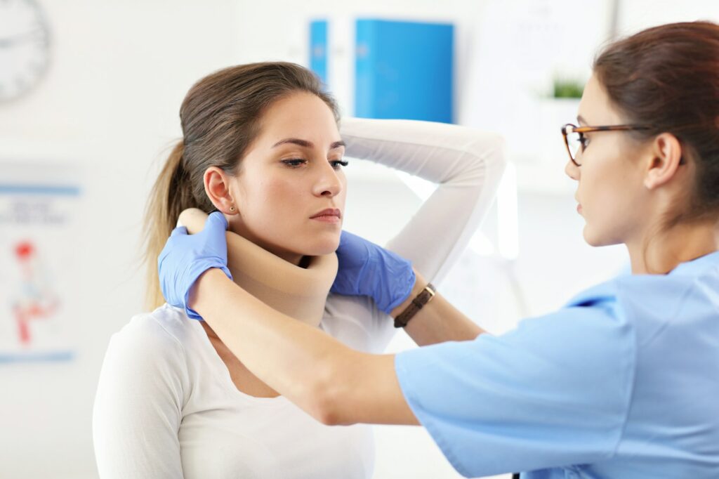 Female doctor putting neck orthopaedic collar on adult injured woman
