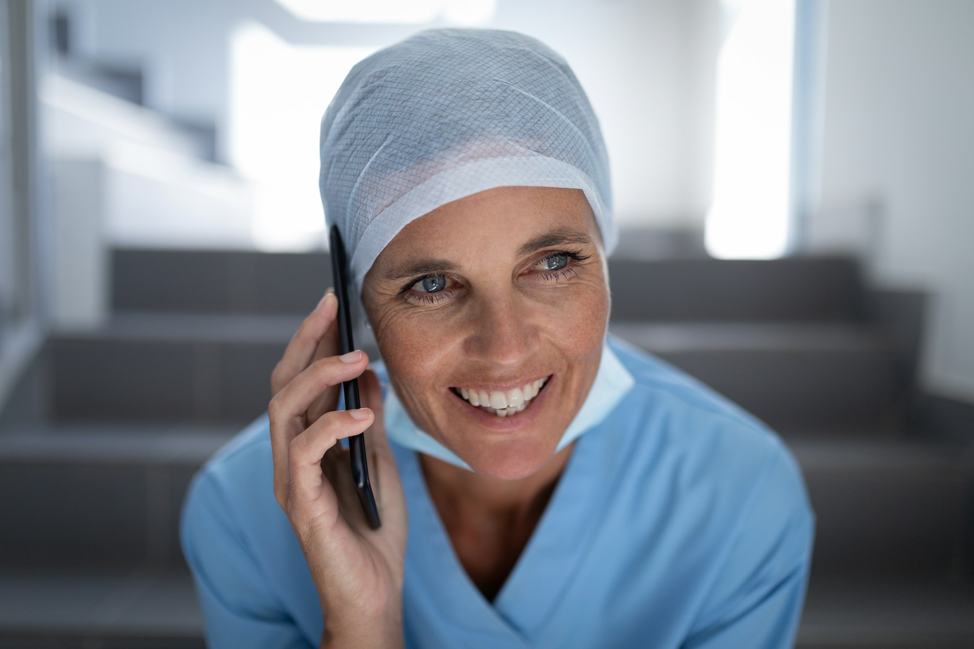 Female surgeon smiling and talking on mobile phone while sitting on hospital stair